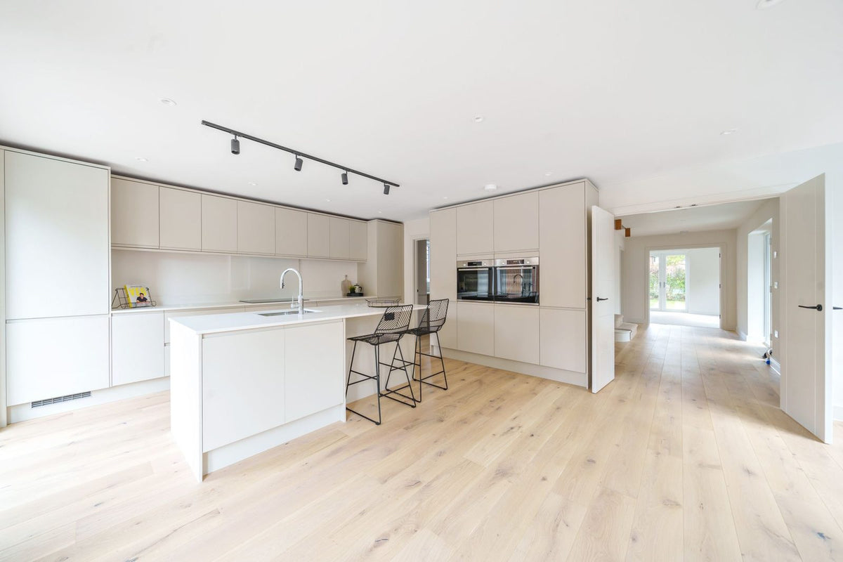The finished kitchen with a white island and bar stools, pale rustic oak planks running through to the hall