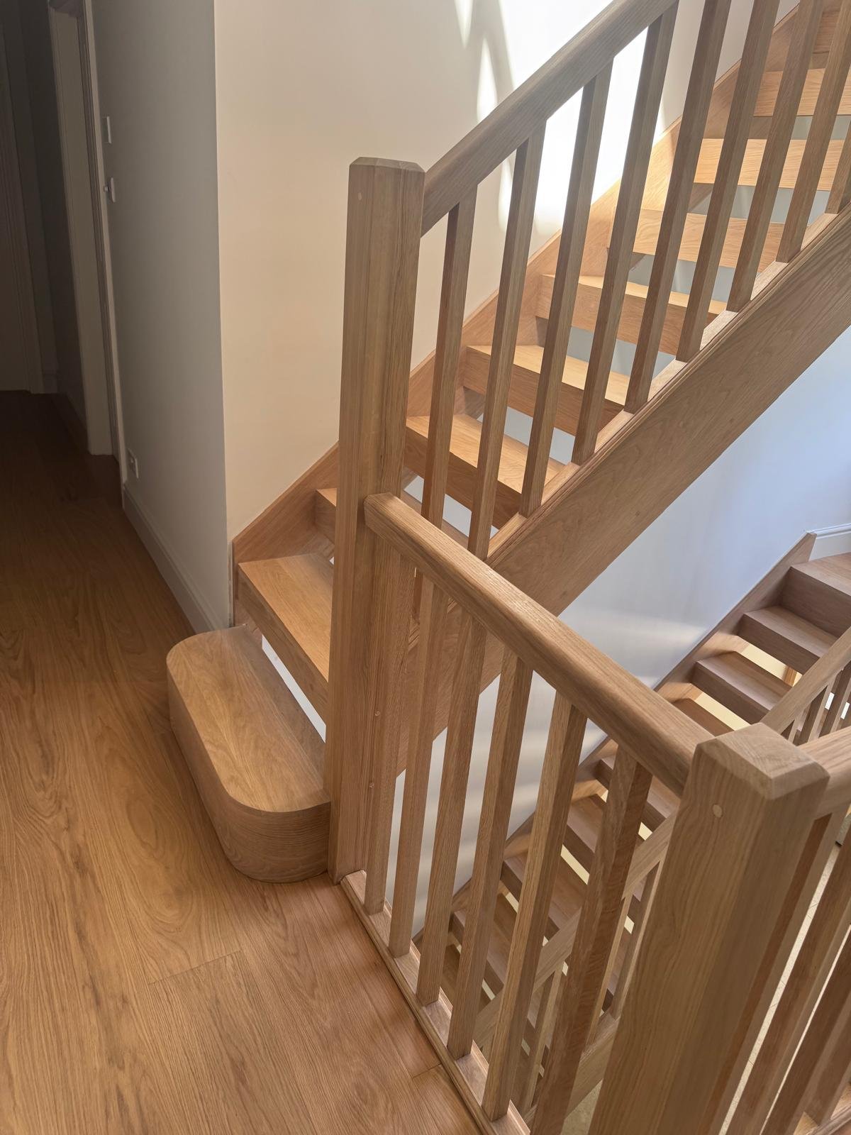 The finished oak staircase from the landing: round-ended bottom step, square spindles and newels, with the plank floor running along the landing