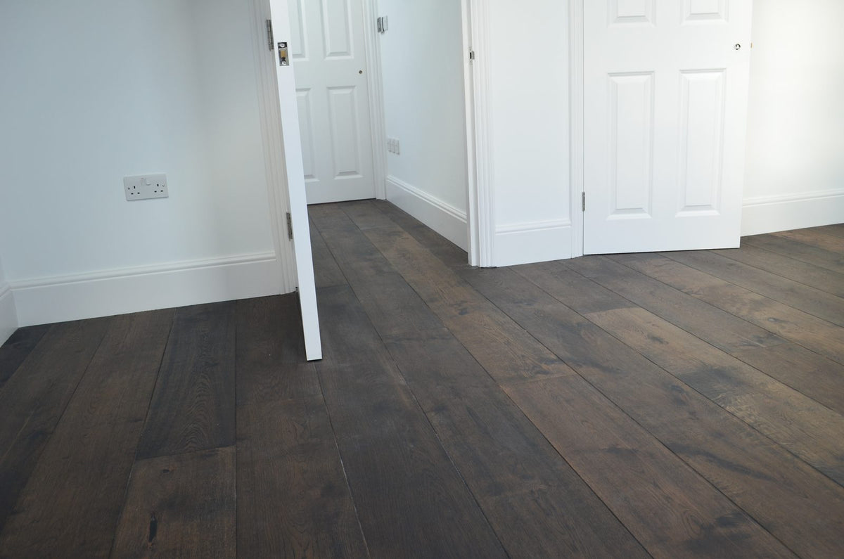A bedroom with white doors and skirting over a very dark brown oak plank floor