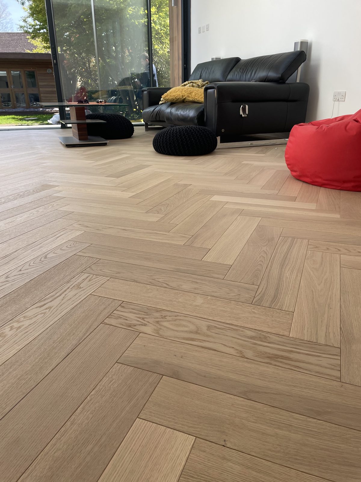 Light oak herringbone in an open-plan room with full-height glazing onto the garden, furnished