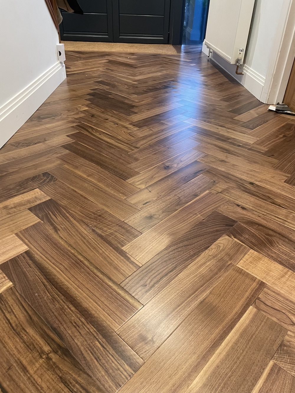 An entrance hall laid in dark brown herringbone running to a coir mat at dark double front doors