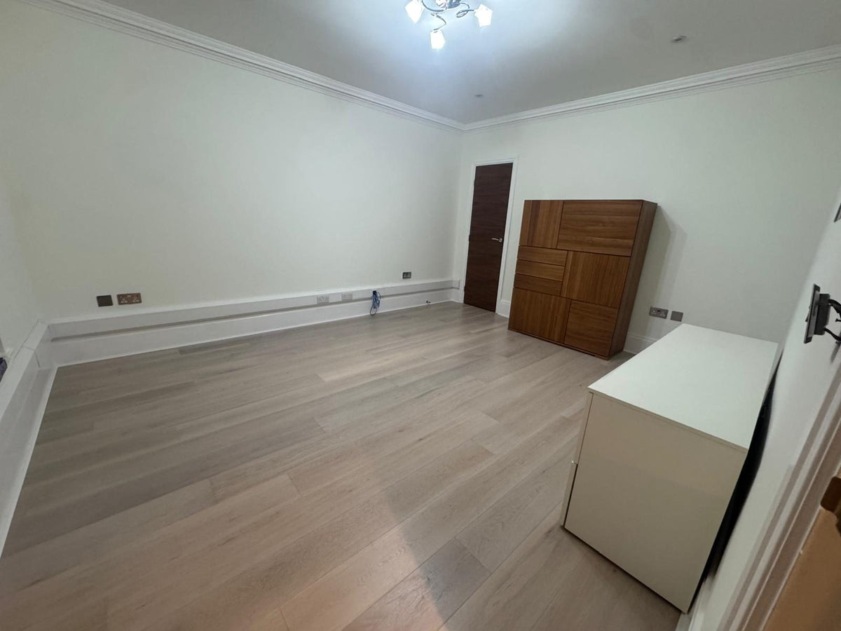 A furnished room with pale grey-washed oak planks, a walnut cabinet and white drawer units