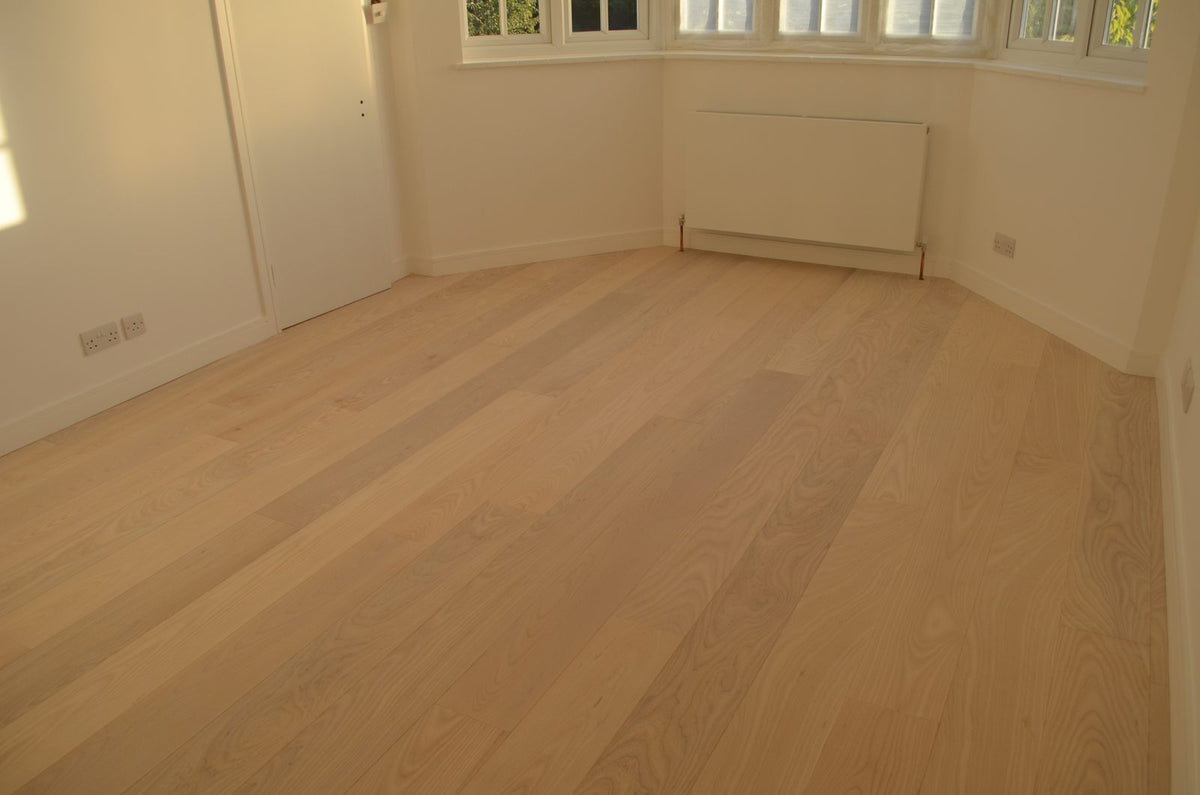 An empty room with a bay window and radiator, floored in pale oak planks, white skirting fitted