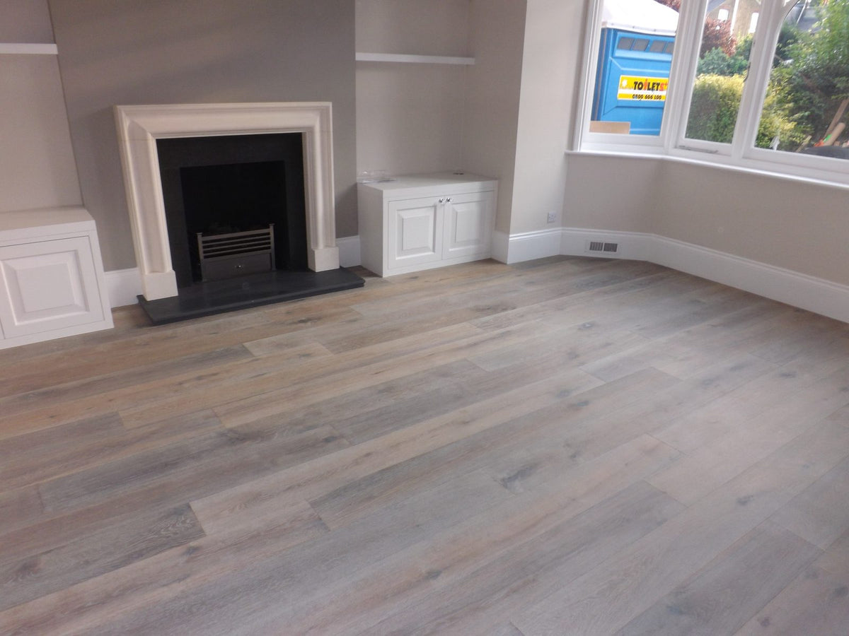 A front reception room with a stone fire surround, alcove cupboards and a bay window, the floor in grey-brown oak planks