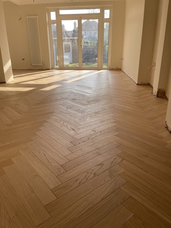 A through lounge laid wall to wall in natural oak herringbone towards French doors, sun across the floor
