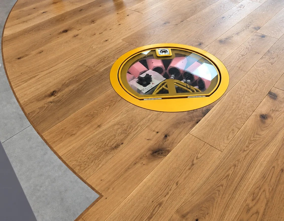 The finished oak floor with the round glass cellar hatch in its yellow frame, and the curved edge where the oak meets grey tiles