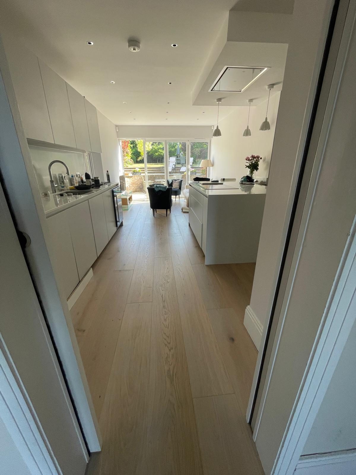 Looking down the kitchen towards the garden doors, the wide oak plank running the length of the room between the units and the island