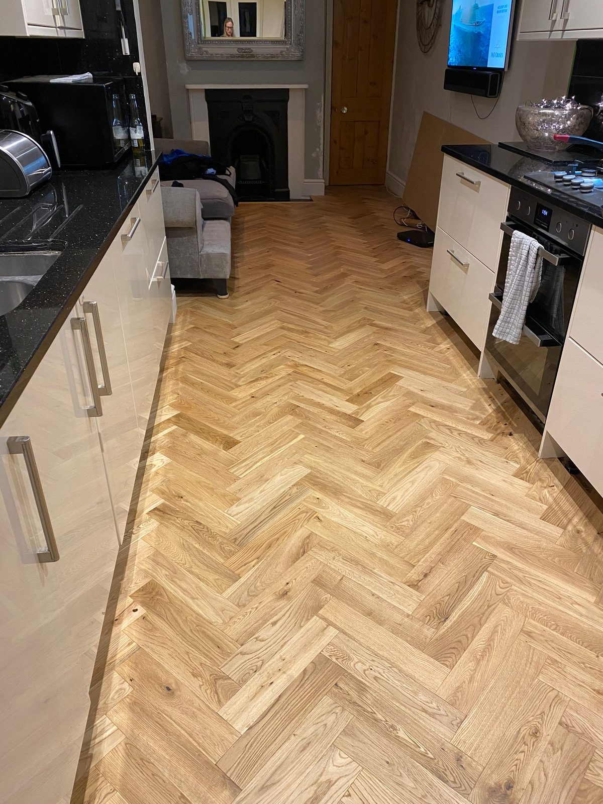 A long kitchen with light rustic oak herringbone running between the units to a cast-iron fireplace at the far end